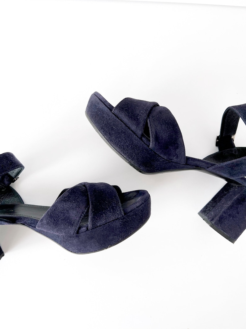 Op de afbeelding: Een paar donkerblauwe su&egrave;de plateau sandalen met enkelbandjes. De sandalen hebben een dikke hak en een gekruist bandje ontwerp.