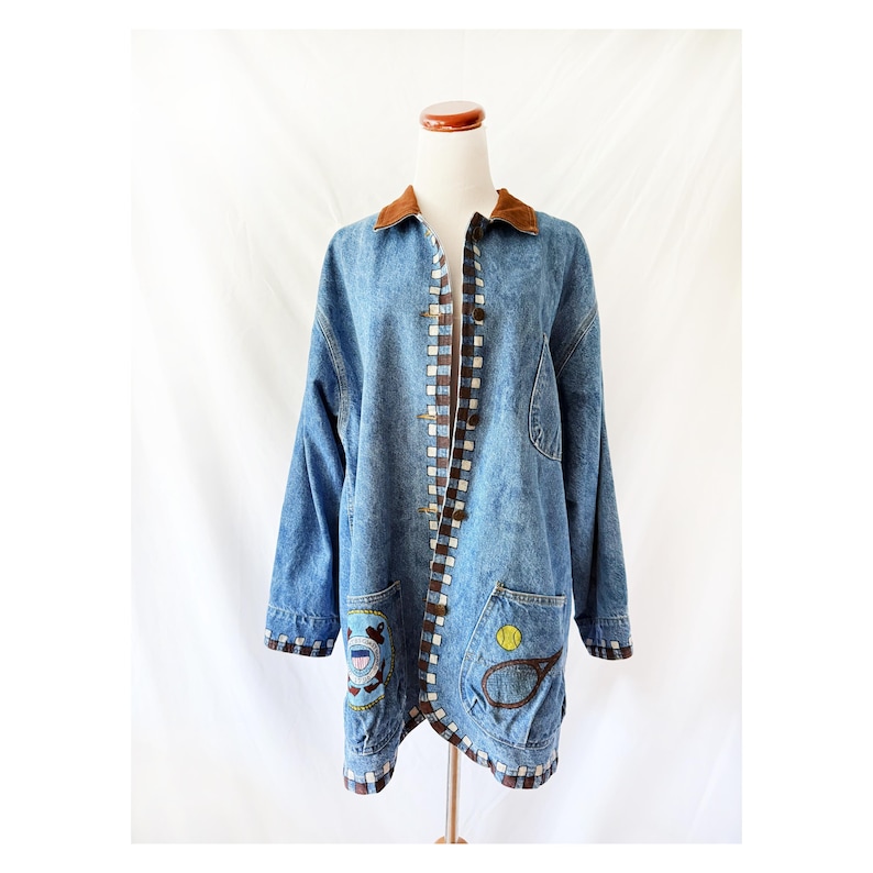 May include: A vintage denim jacket with a brown corduroy collar and trim. The jacket features two front pockets with embroidered sports-themed patches. The jacket is displayed on a mannequin against a white backdrop.