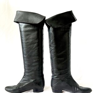 May include: A pair of black leather over-the-knee boots with a folded-over cuff at the top. The boots have a low heel and a pointed toe.