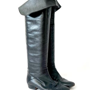 May include: A pair of black leather knee-high boots with a folded-over top and a low heel.