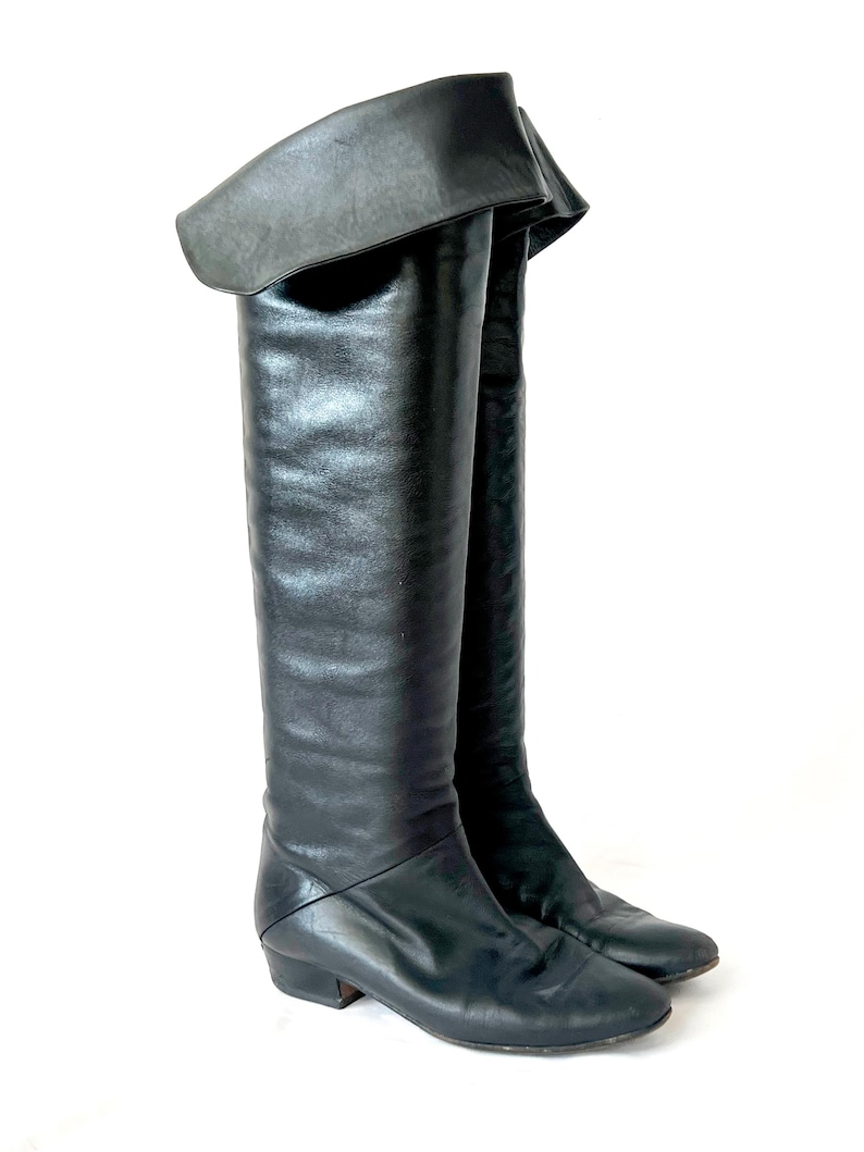 May include: A pair of black leather knee-high boots with a folded-over top and a low heel.