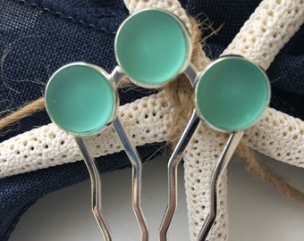 May include: Three silver hair combs with turquoise blue glass accents. The combs have a wavy design and are arranged in a star shape.