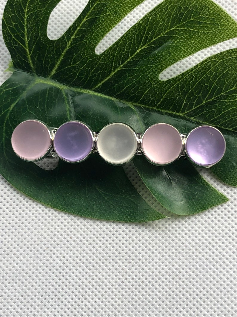 May include: A silver hair clip with five round, translucent stones. The stones are in shades of purple, pink, and white.