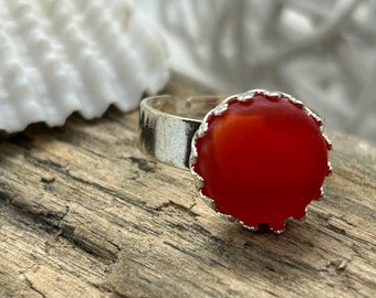 May include: A silver ring with a red, round, glass stone set in a scalloped bezel.
