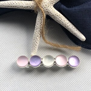 May include: A silver hair clip with five round iridescent stones. The stones are pink, purple, white, pink, and purple.