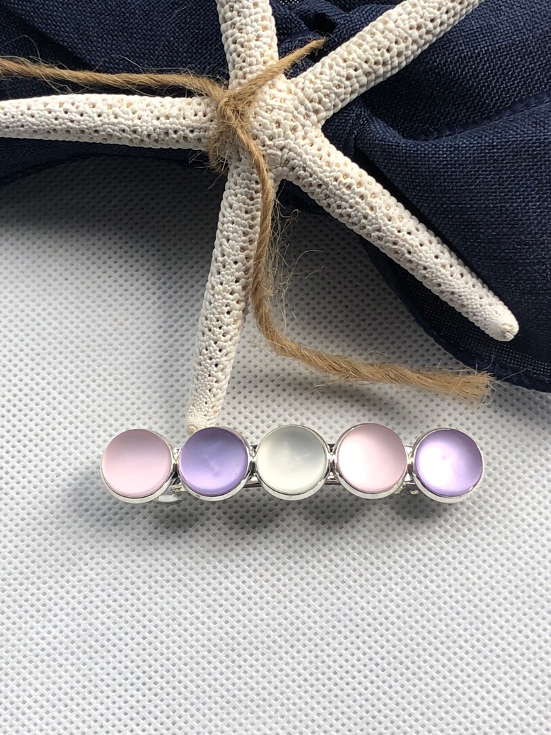 May include: A silver hair clip with five round iridescent stones. The stones are pink, purple, white, pink, and purple.