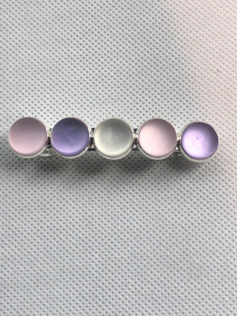 May include: A hair clip with five round, iridescent, pastel-colored stones. The stones are arranged in a row and are set in silver.