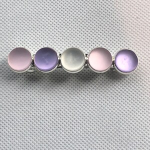 May include: A silver bar with five round, iridescent stones. The stones are in a gradient of pink, purple, white, pink, and purple.