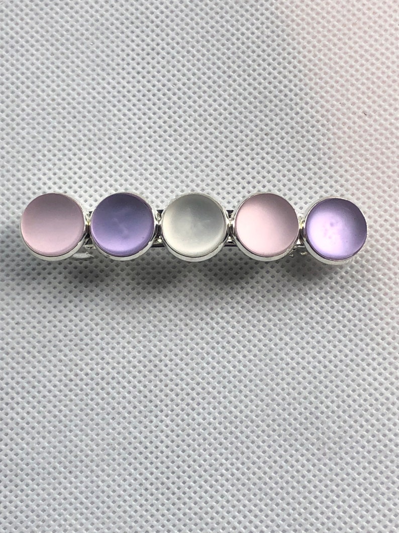 May include: A silver bar with five round, iridescent stones. The stones are in a gradient of pink, purple, white, pink, and purple.