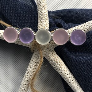 May include: A silver hair clip with five round glass stones. The stones are in shades of purple and white.