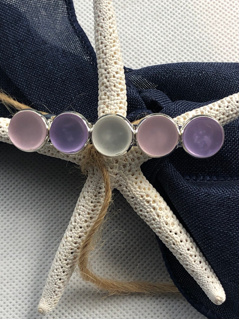 May include: A silver hair clip with five round glass stones. The stones are in shades of purple and white.