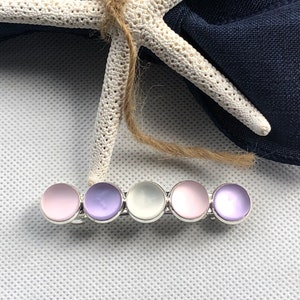 May include: A hair clip with five iridescent round stones in shades of pink, purple, and white. The stones are set in a silver metal bar.