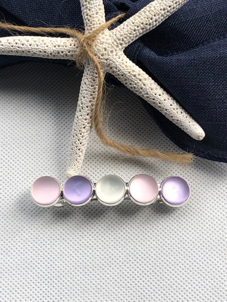 May include: A hair clip with five iridescent round stones in shades of pink, purple, and white. The stones are set in a silver metal bar.