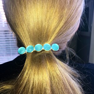 May include: A silver hair clip with five turquoise blue round stones. The stones are set in a row on the clip.