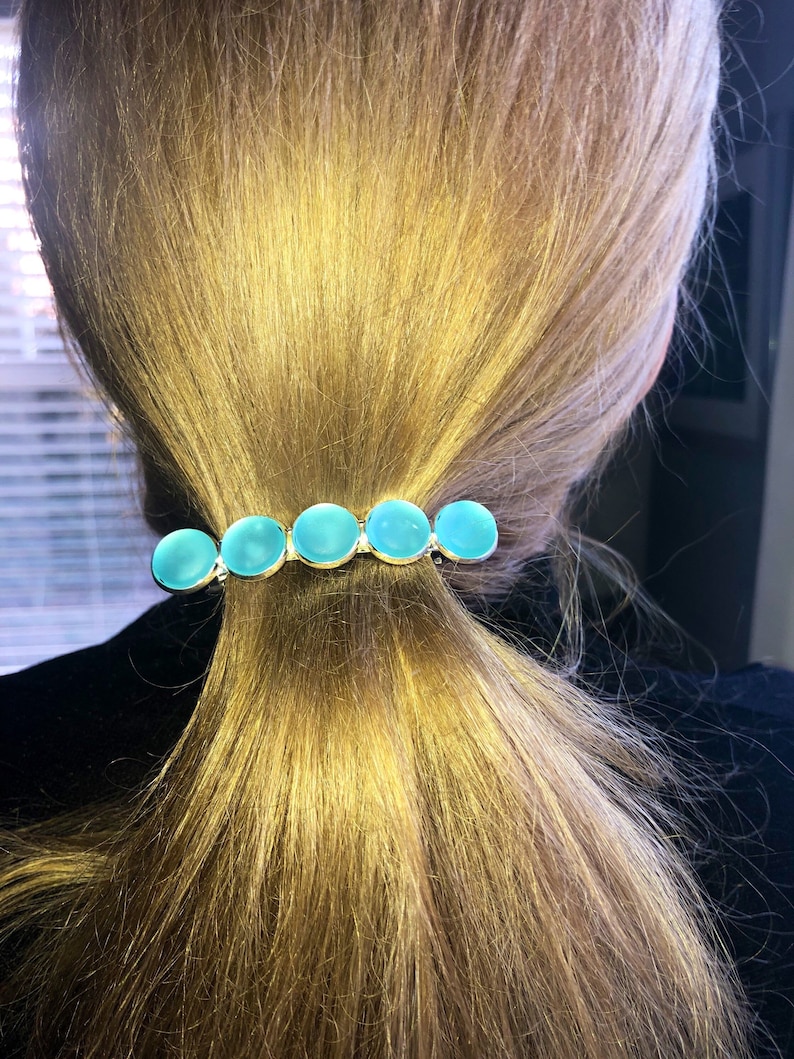 May include: A silver hair clip with five turquoise blue round stones. The stones are set in a row on the clip.
