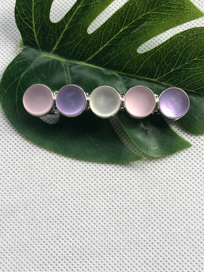 May include: A silver hair clip with five round, iridescent stones. The stones are in shades of pink, purple, and white.