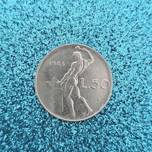 Könnte beinhalten: Eine italienische Silbermünze mit einem Mann, der einen Hammer hält, und dem Text "1965 L.50".