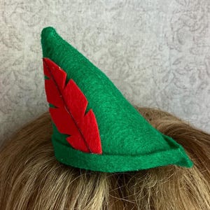 May include: A green felt hat with a red feather attached. The hat is a pointed shape, and the feather is a bright red color. The hat is likely a costume accessory.