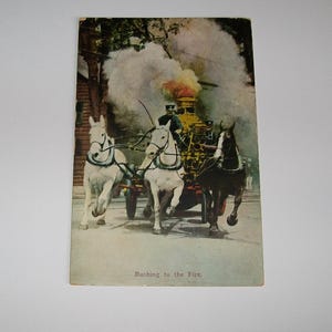 May include: A vintage postcard titled Rushing to the Fire, depicting a horse-drawn steam fire engine with two white horses and one dark horse pulling the apparatus. A driver in a dark uniform sits atop the gold-toned engine emitting smoke.