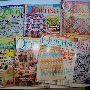 May include: A collection of American Patchwork & Quilting magazines. The covers feature colorful quilt designs, with titles like "Sew Easy" and "Color Sense." The magazines are stacked, showcasing various quilting techniques and patterns.