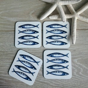 May include: Set of four white square coasters with a blue and white illustration of mackerel fish. Each coaster features four fish in a row.