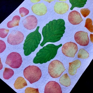 May include: A white background with a pattern of pink and yellow flower petals and green leaves. The petals are arranged in a circle around the leaves.