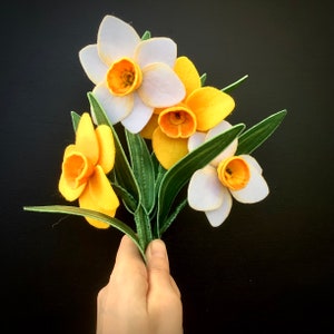 May include: A bouquet of felt daffodils in shades of yellow and white. The flowers are arranged in a hand-tied bunch with green felt leaves.