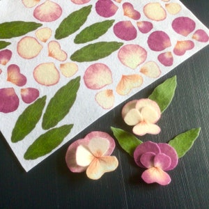 Peut inclure: Une feuille de papier avec des pétales de fleurs en feutre rose et blanc et des feuilles vertes. Trois fleurs en feutre sont disposées sur une surface noire. Les fleurs sont faites de pétales de feutre rose et blanc.