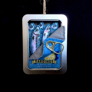 May include: A silver tin can with a blue and white label that reads "Sardines in Olive Oil and Lemon". The can is open and there are five sardines inside. The sardines are made of felt and have realistic details.