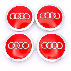 Könnte beinhalten: Vier rote und silberne Radnabenabdeckungen. Jede Kappe zeigt das Audi-Logo, ein Satz von vier ineinandergreifenden Ringen, in Silber auf rotem Hintergrund. Die Kappen haben eine glänzende, reflektierende Oberfläche.