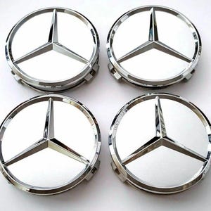Puede incluir: Cuatro tapacubos Mercedes-Benz plateados y blancos. Cada tapacubo presenta el icónico emblema de la estrella de tres puntas en el centro, rodeado por un anillo plateado pulido. Los tapacubos están diseñados para adaptarse a las ruedas de los coches.