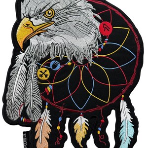 May include: Embroidered patch featuring a white-headed eagle with yellow beak and eyes, surrounded by a colourful dreamcatcher with feathers hanging down. The dreamcatcher is red, blue, yellow, and black. The patch has the text "Wolfclaws" on the bottom left corner.
