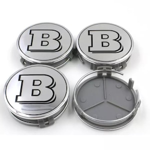 May include: Four silver hubcaps featuring a black outlined "B" logo. One hubcap is detached, showing a grey plastic backing. The circular hubcaps have a metallic finish, ideal for car modifications.