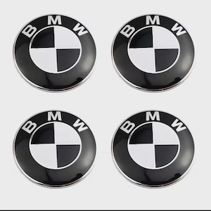 May include: A set of four circular BMW emblems featuring a black outer ring with the white letters B, M, and W printed at the top. The centre of each emblem displays a quadrant design alternating between white and black sections with a glossy finish.