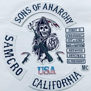 Puede incluir: Un parche blanco con texto negro que dice "Sons of Anarchy" en un arco curvo. Debajo del arco hay una imagen en blanco y negro de una figura encapuchada sosteniendo un rifle. La figura está rodeada de parches más pequeños con texto que dice "Samcro", "USA", "California", "First 9", "President", "Sgt at Arms", "Men of Mayhem", "Redwood", "Original", "V. President" y "MC".