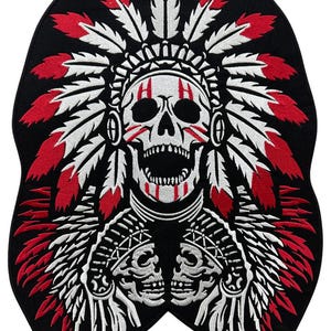 Op de afbeelding: Zwarte en witte geborduurde patch van een schedel die een rode en witte verenhoofdtooi draagt. De schedel heeft rode verfmarkeringen op zijn gezicht en houdt twee kleinere schedels in zijn handen.
