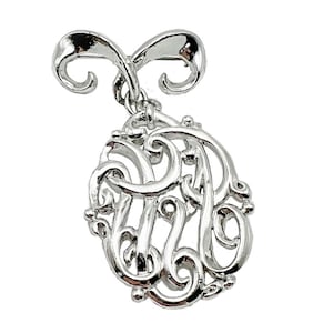 May include: Silver-toned monogram brooch with a decorative, ornate design. The brooch features a stylized letter 'A' with intricate swirls and flourishes.