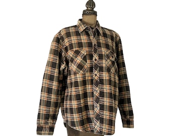 May include: A long-sleeved, button-down flannel shirt in a plaid pattern. The shirt features a color palette of brown, black, orange, and beige. It has two chest pockets and a classic collar. The shirt is displayed on a mannequin.