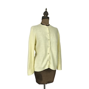May include: A pale yellow cardigan sweater with a button-up front. The sweater is made of a soft, fuzzy material.