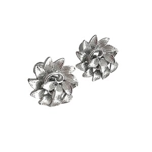 Puede incluir: Un par de pendientes de plata en forma de flor. Los pendientes están hechos de metal y tienen un diseño delicado e intrincado.