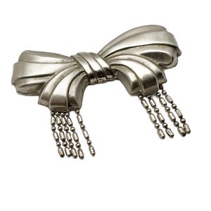May include: A silver bow brooch with a dangling chain of beads.