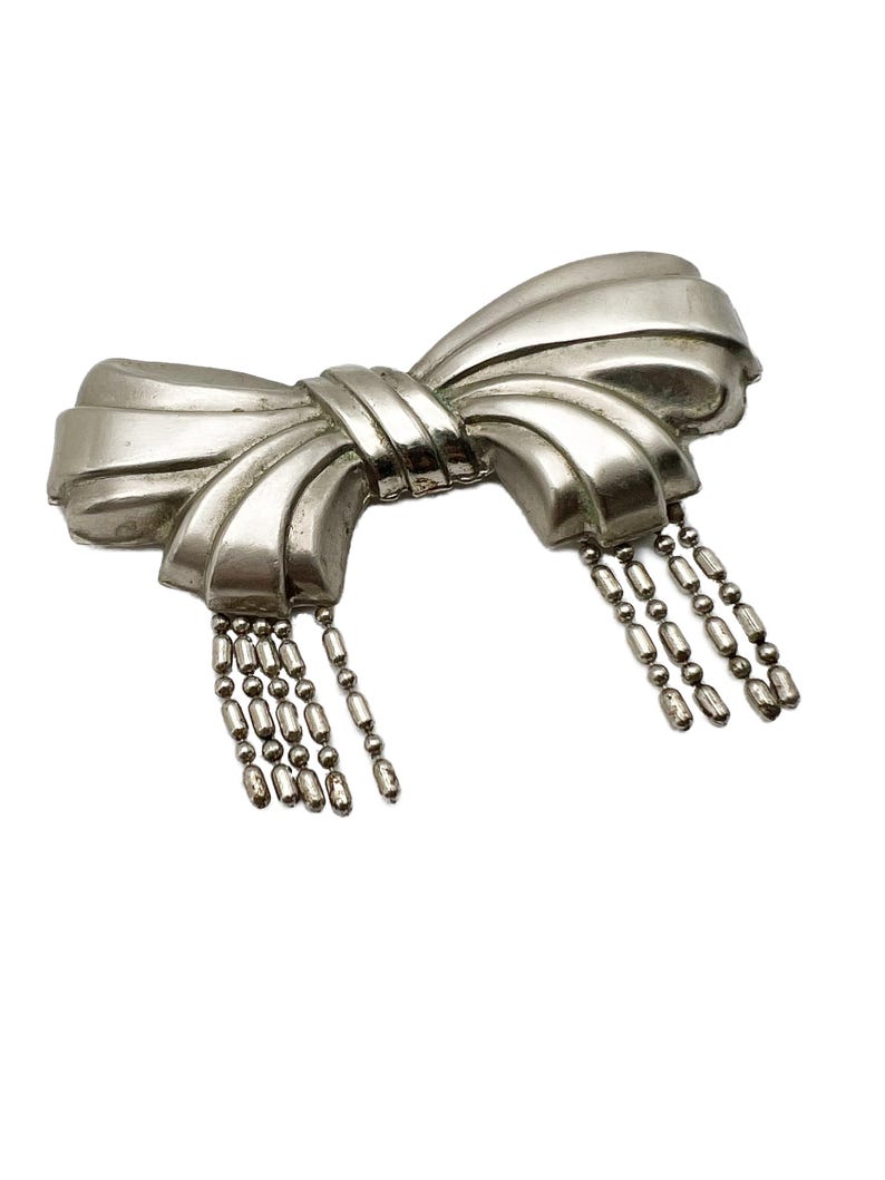 May include: A silver bow brooch with a dangling chain of beads.