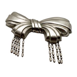 May include: A silver bow brooch with a dangling chain of beads.