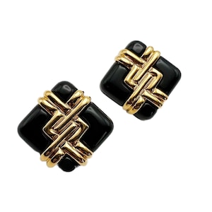 Puede incluir: Un par de pendientes cuadrados negros y dorados con un diseño geométrico. Los pendientes están hechos de esmalte negro y metal dorado.