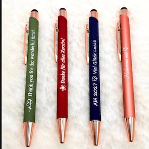 Könnte beinhalten: Vier Stifte in Grün, Rot, Blau und Koralle. Jeder Stift hat einen roségoldenen Clip und eine Spitze. Der grüne Stift lautet "Thank you for the wonderful time!". Der rote Stift lautet "Danke für alles Kerstin!". Der blaue Stift lautet "Abi 2027 Viel Glück Lucas!". Der korallenfarbene Stift lautet "Hebamme mit".