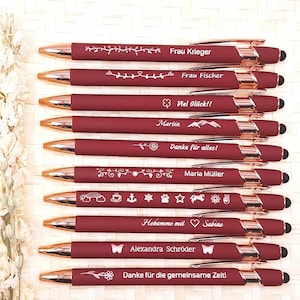 Könnte beinhalten: Eine Sammlung weinroter Stifte mit roségoldenen Akzenten. Jeder Stift hat eine einzigartige weiße Gravur, darunter Namen und Sätze wie "Frau Krieger" und "Viel Glück!!". Die Stifte haben eine Stylus-Spitze.