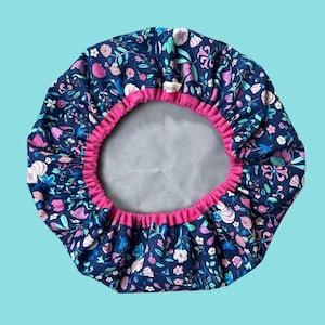 May include: A blue and pink floral shower cap with a pink elastic band. The cap is made of fabric and has a white lining.