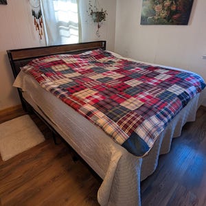 May include: A bed with a dark wooden headboard and a metal frame. The bed is covered with a patchwork quilt in red, blue, and green plaid patterns. A white quilted bedspread and a small white rug are also visible.
