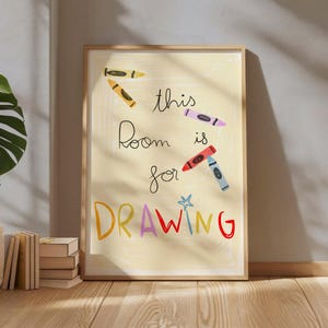 Puede incluir: Un estampado enmarcado con un fondo amarillo claro y un marco de madera. El estampado presenta las palabras "this Room is for DRAWING" en una fuente lúdica, junto con ilustraciones de crayones de colores. La obra de arte se exhibe sobre un suelo de madera.