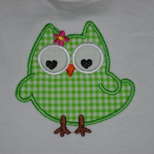 May include: Green owl with white eyes and black hearts, a pink flower on its head, and a green and white gingham pattern on its body.
